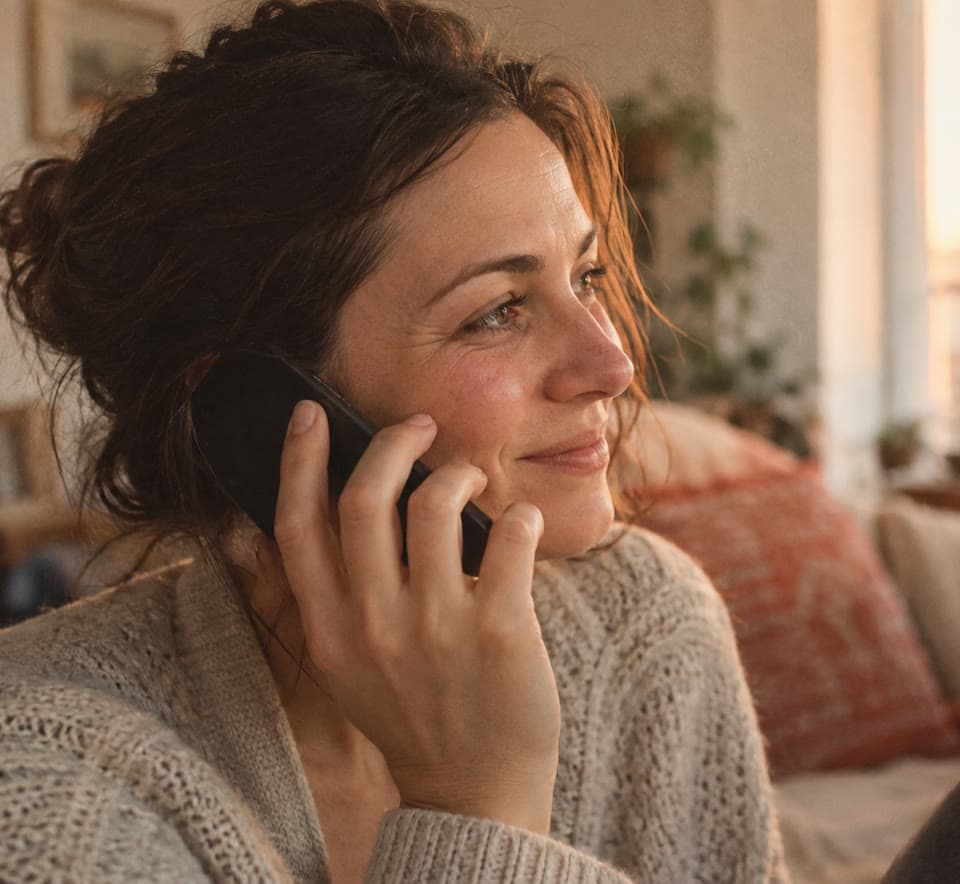 A woman smiling softly while talking with her mom on the phone